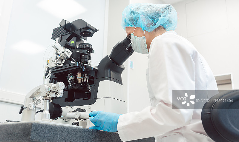 在医学实验室工作的有操作器和显微镜的女医生图片素材
