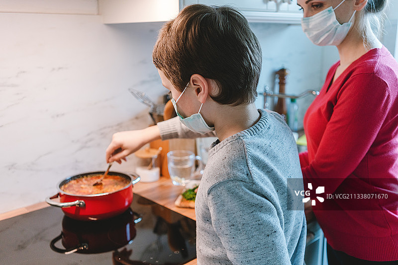 母亲和儿子在家里一起做饭，戴着口罩在厨房里图片素材