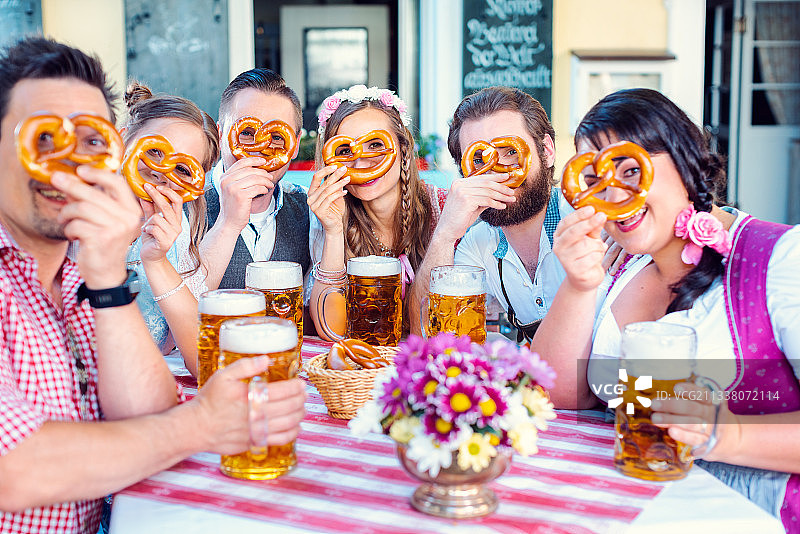 在巴伐利亚啤酒花园的一群人透过摄像机的椒盐卷饼洞看着图片素材