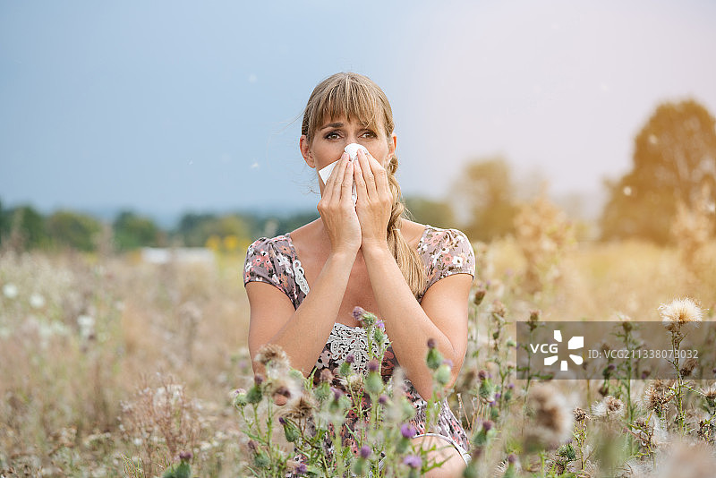 一个女人坐在干草草地上，用手帕捂着鼻子图片素材