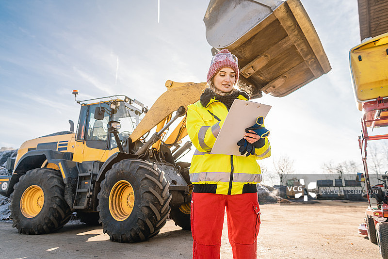 女人拿着写字板在建筑机械前写字图片素材