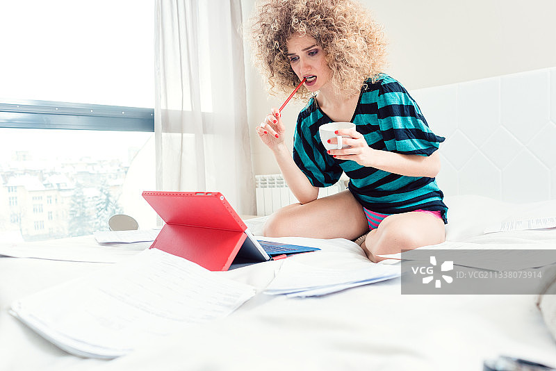 一个女人在床上工作，手提电脑看起来很困惑图片素材