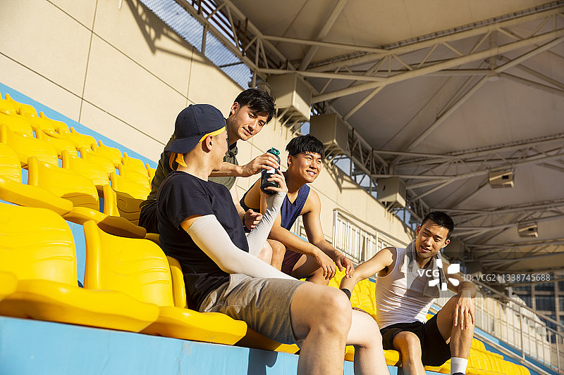 四个青年男子准备打篮球坐在学校操场看台休息图片素材