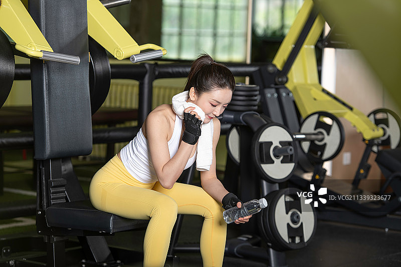 健身的年轻女性，在健身房训练间隙喝水、休息。身材健美的年轻女人图片素材