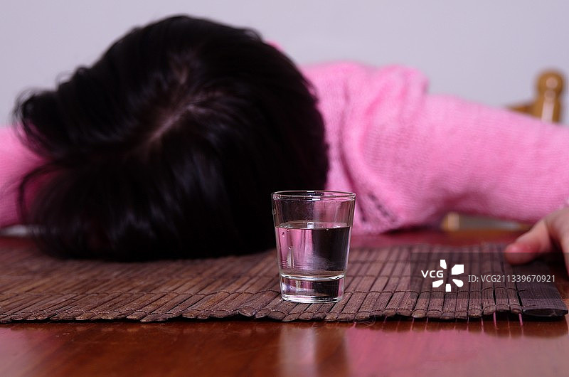 女人醉倒在桌子上，旁边有一杯酒图片素材