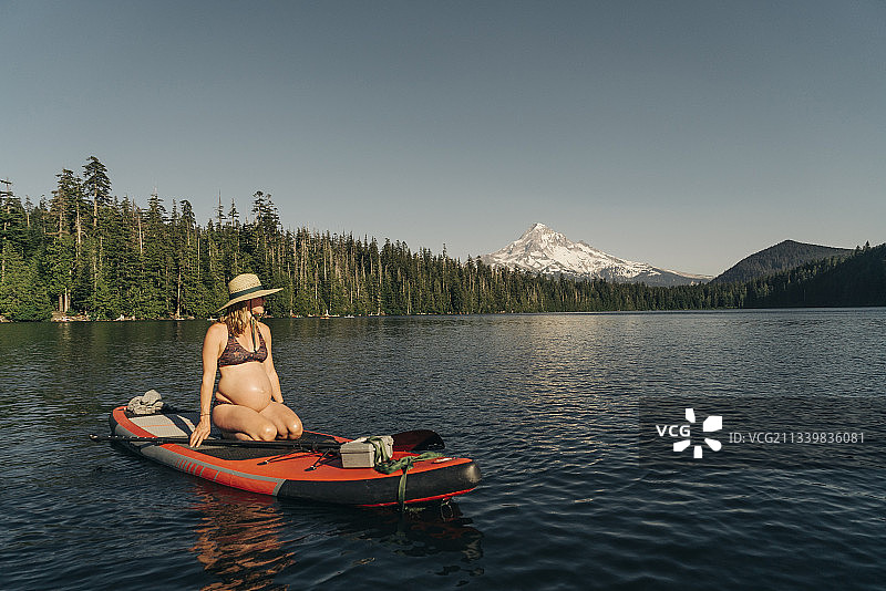 在胡德山附近的俄勒冈州高山湖泊上坐在桨板上的年轻孕妇图片素材