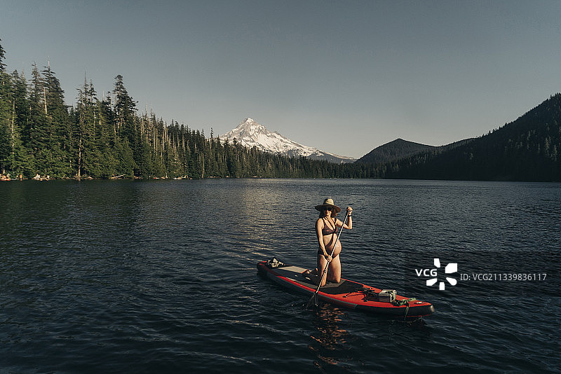 在胡德山附近的俄勒冈州高山湖泊上坐在桨板上的年轻孕妇图片素材