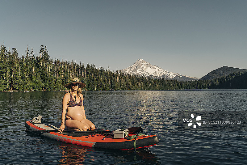 在胡德山附近的俄勒冈州高山湖泊上坐在桨板上的年轻孕妇图片素材