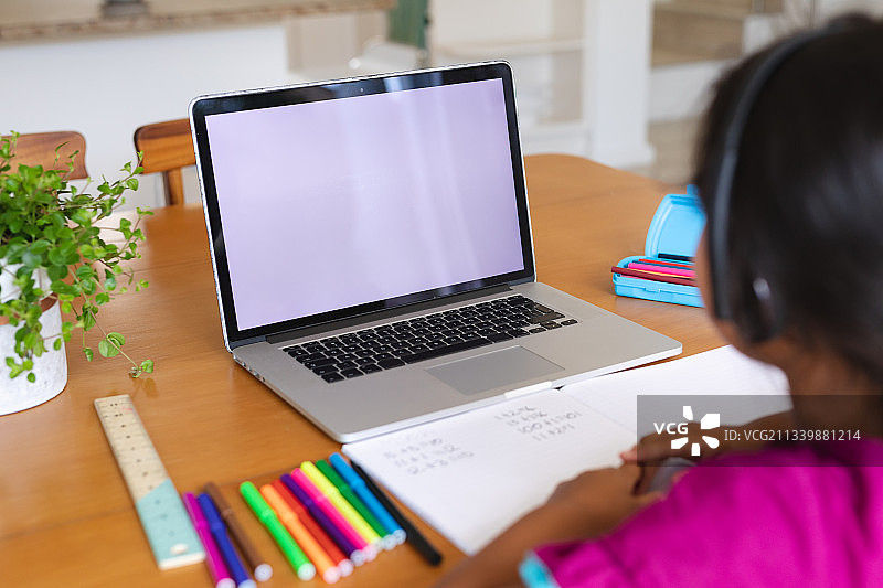 西班牙裔女孩戴着耳机，在网课中使用带复制空间的笔记本电脑图片素材