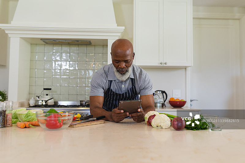 年长非裔美国人在厨房用平板电脑做饭图片素材