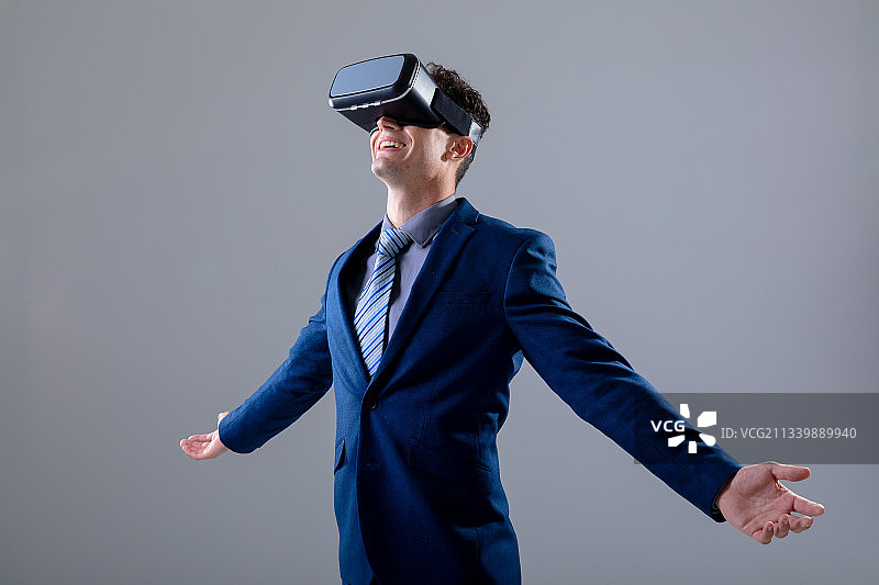 戴着VR头显，张开双臂的白人商人，在灰色背景下图片素材