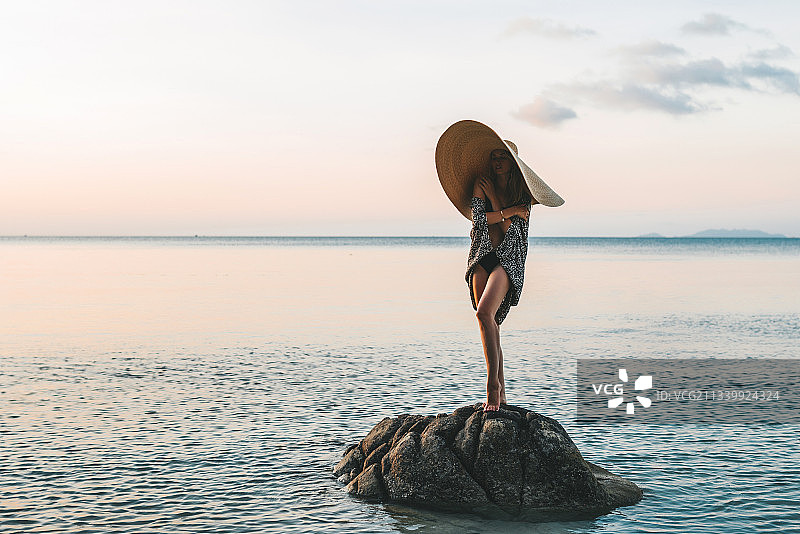 日落时分站在泰国帕岸岛海滩岩石上的女人图片素材