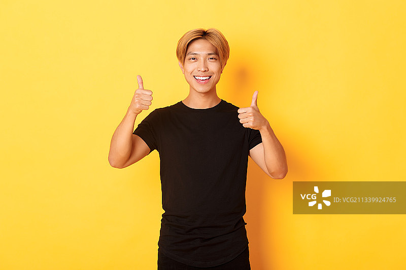 站在黄色背景前做手势的年轻微笑女性图片素材