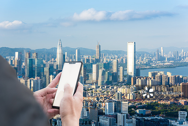 拿着手机的手和深圳南山区城市天际线图片素材