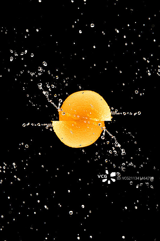 黑色背景下带着水珠高速旋转的橙子图片素材