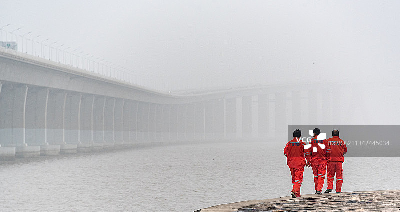 雾气中的上海长江大桥向远方延伸，穿制服的工程人员沿着江提巡逻图片素材