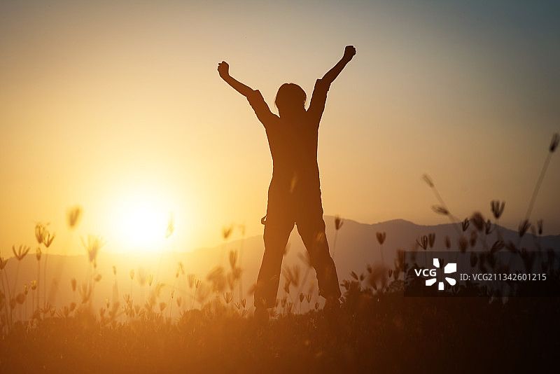日落时分，站在田野上举起双臂的男人剪影图片素材