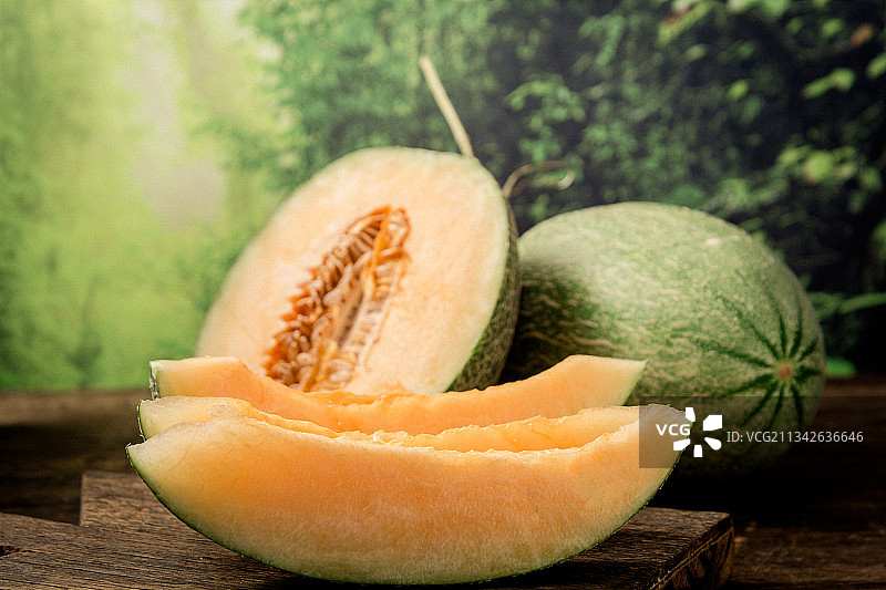 绿色森系背景前木纹桌子上切开的哈密瓜图片素材