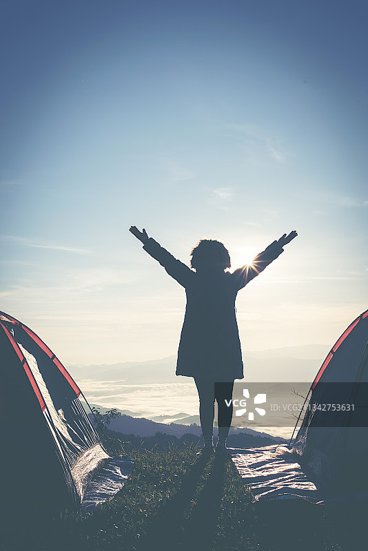 快乐的年轻女登山者在山顶日落时张开双臂图片素材