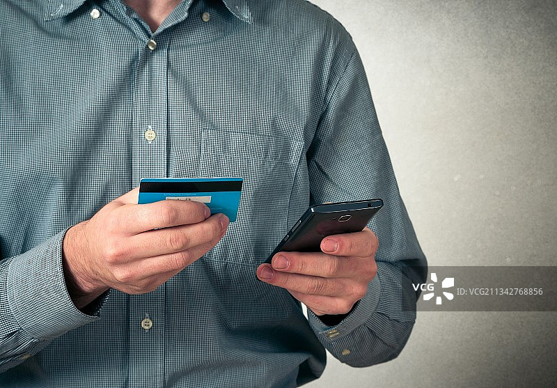 男子拿着信用卡使用手机的中段图片素材