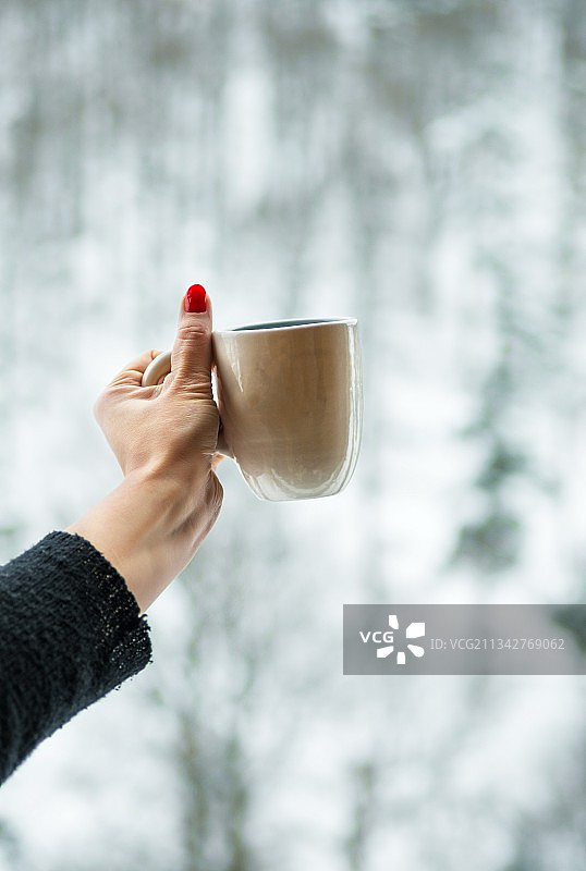 女子手持咖啡杯，背景是树木图片素材