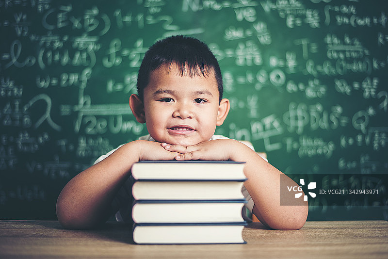 可爱的男孩的肖像和书在上对着黑板图片素材