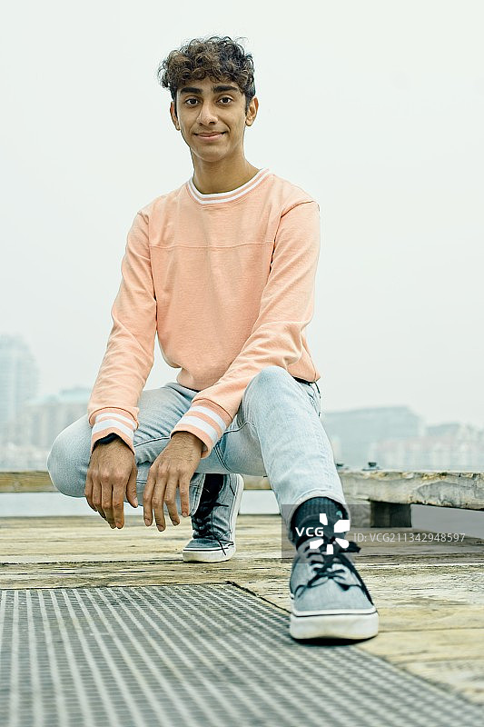 年轻男子坐在加拿大不列颠哥伦比亚省维多利亚市的栏杆上，背景是晴朗的天空的肖像照图片素材