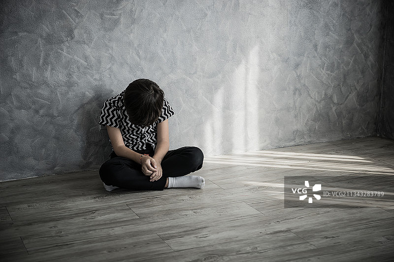 悲伤的年轻男孩靠墙坐在地板上图片素材