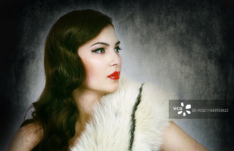 年轻女子穿着皮草大衣，靠在纹理墙上图片素材