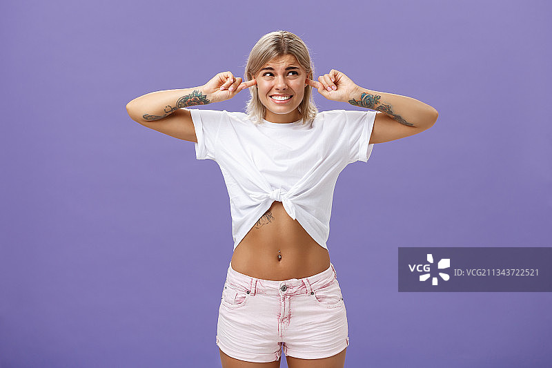 站在紫色背景前，用手指堵住耳朵的妇女肖像图片素材