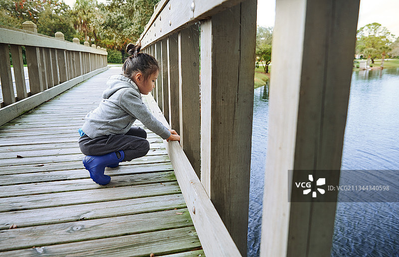 可爱的女孩穿着橡胶靴在郊区池塘上的木桥上玩耍图片素材