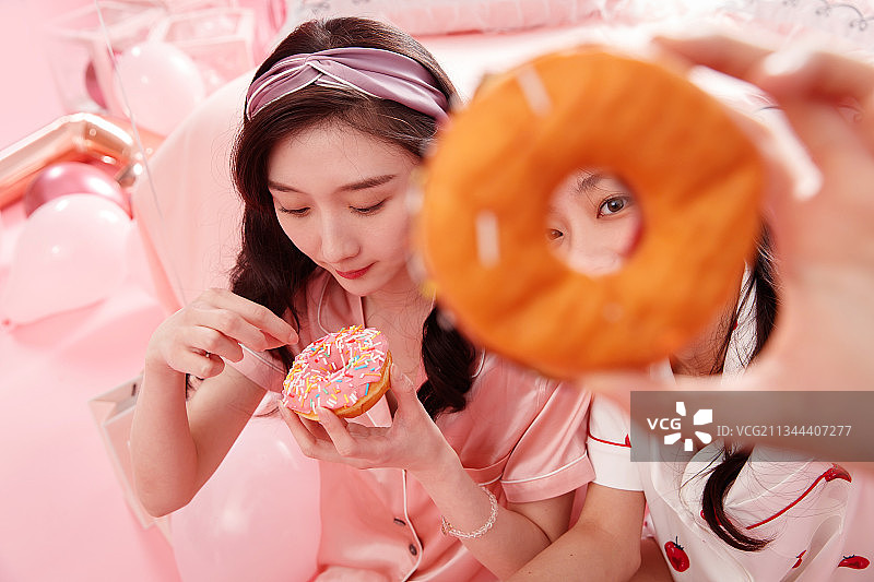 拿着甜甜圈的漂亮年轻闺蜜图片素材