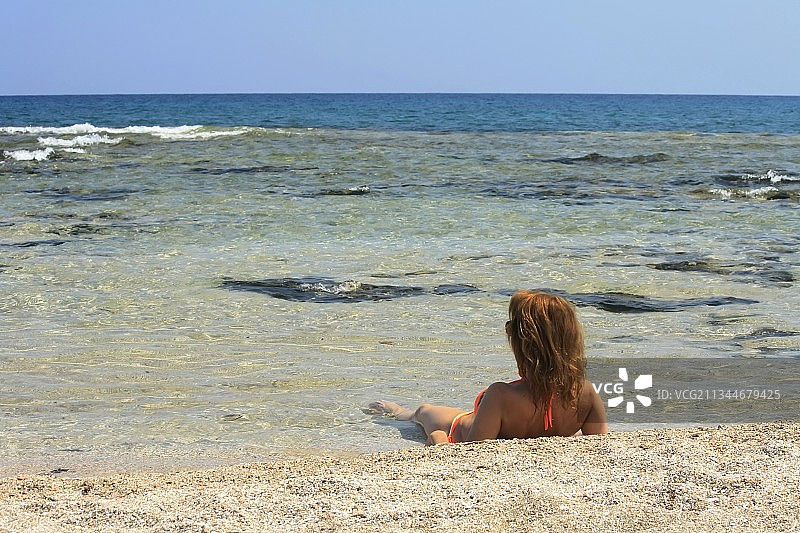 女子坐在海滩上对着晴朗天空的背影图片素材