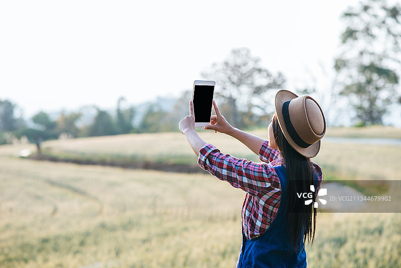站在田野上使用平板电脑的女子背影图片素材