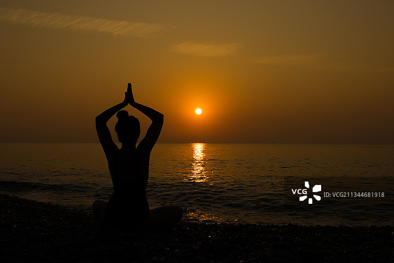 日落时分，意大利卡坦扎罗Roccelletta海滩上做瑜伽的女子剪影图片素材