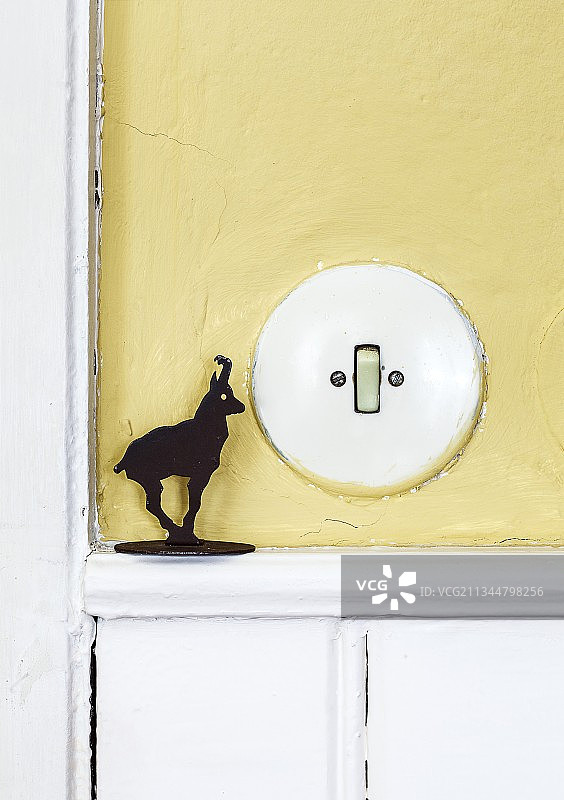 淡黄色墙壁上的老式胶木灯开关和小羚羊雕像图片素材