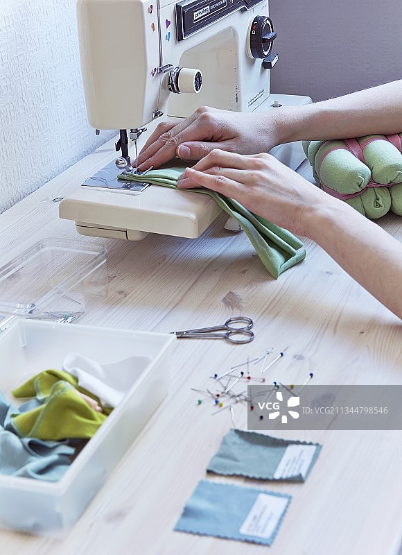 缝纫机旁的彩色布料样品和别针；女人手持缝纫机针下的布料图片素材