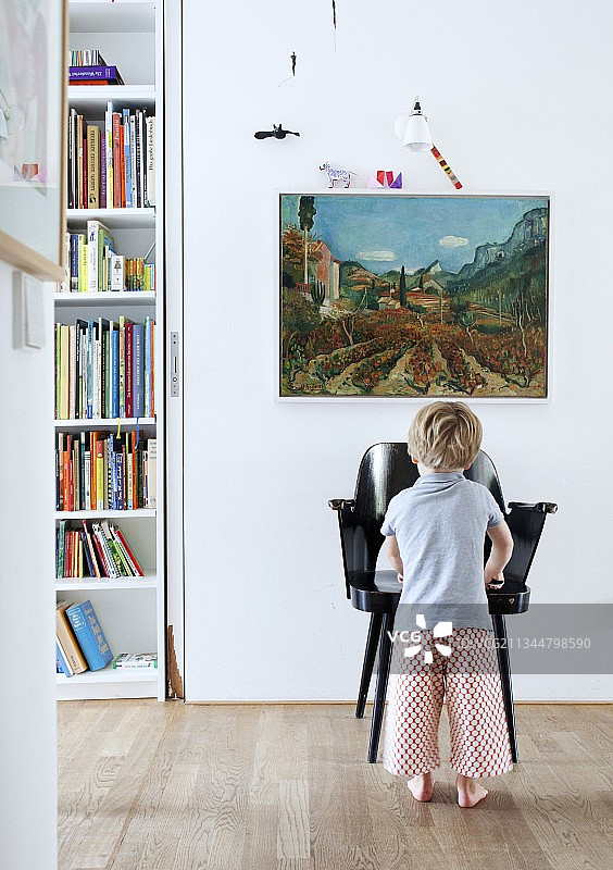 幼儿站在黑色扶手椅前，墙上挂着风景画图片素材