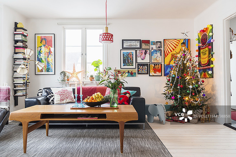 客厅一角：黑色皮沙发前的咖啡桌，圣诞树与漫画风装饰画图片素材