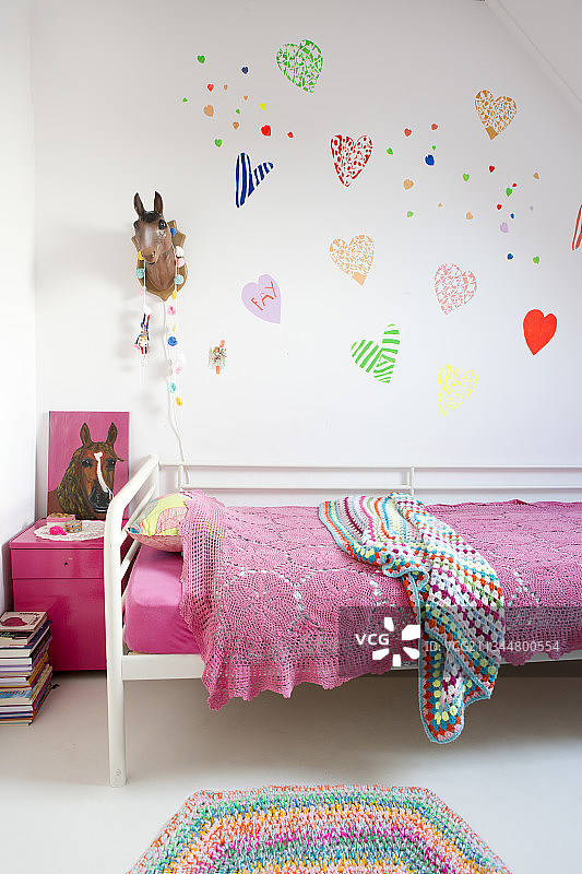 女孩卧室墙上床头挂着用粉红色花边毯子盖着的彩色爱心图片素材