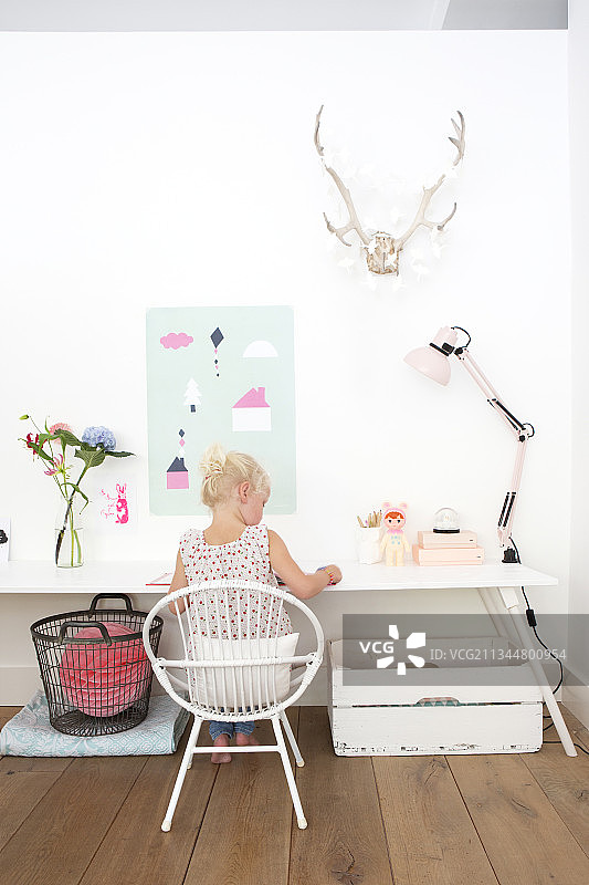 女孩坐在白色桌子旁，墙上有狩猎战利品和纸质装饰品图片素材