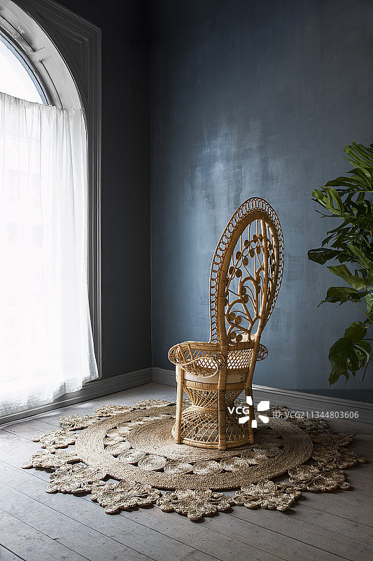 深蓝色墙壁旁拱形窗户边的剑麻地毯上的孔雀椅图片素材