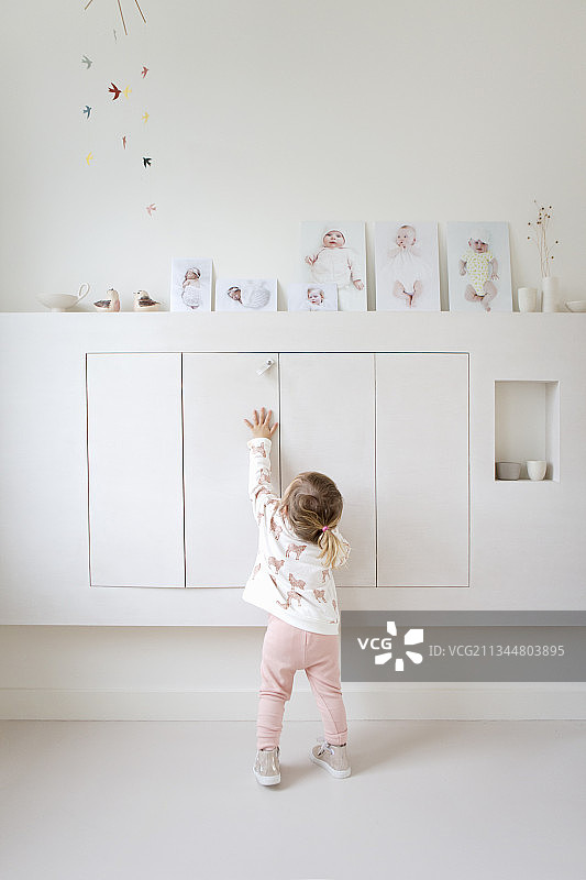 小女孩站在浮动柜子前，柜子上放着婴儿照片图片素材