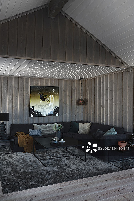 带木镶板墙壁和天花板的黑暗客厅中的黑色转角沙发图片素材