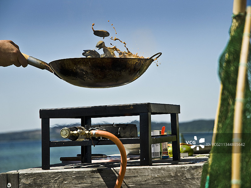 在海滩上，食物在燃气灶上的炒锅中翻炒图片素材