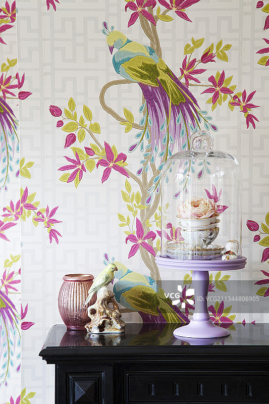 玻璃罩下的茶杯玫瑰与小鸟摆件，背景是小鸟图案壁纸图片素材