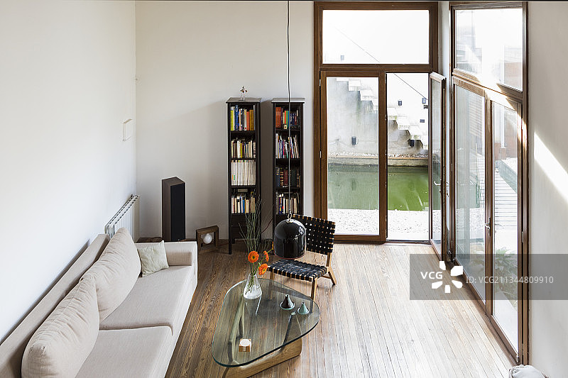 客厅里法式落地窗旁的浅色沙发、玻璃桌和书架图片素材
