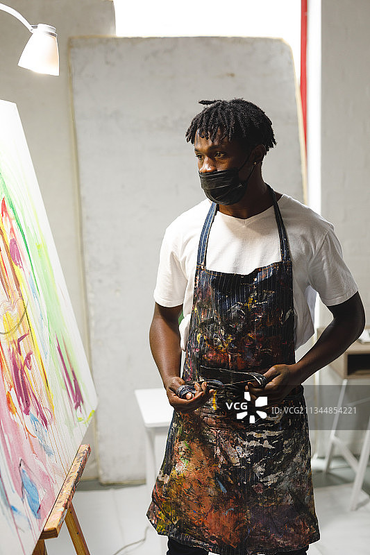 戴着口罩的非洲裔美国男画家在艺术工作室的画布上绘画图片素材
