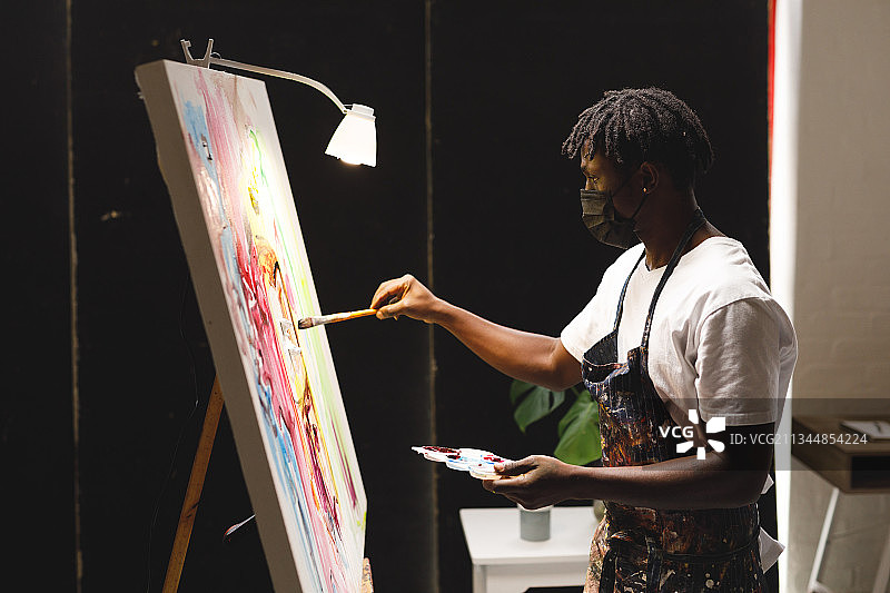 戴着口罩的非洲裔美国男画家在艺术工作室的画布上绘画图片素材