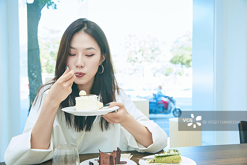 在烘焙店吃蛋糕喝饮料的可爱亚洲少女图片素材